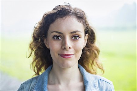 A young woman in a rural landscape, with windblown curly hair, smiling. Stock Photo - Premium Royalty-Free, Code: 6118-07235182