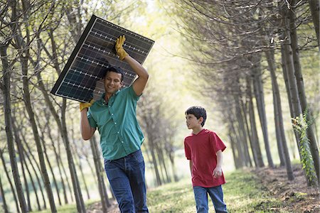 simsearch:6118-08827479,k - A man carrying a solar panel down an avenue of trees, accompanied by a child. Stockbilder - Premium RF Lizenzfrei, Bildnummer: 6118-07235105