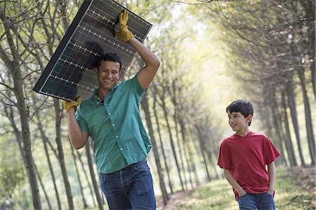 simsearch:6118-07235109,k - A man carrying a solar panel down an avenue of trees, accompanied by a child. Photographie de stock - Premium Libres de Droits, Code: 6118-07235106