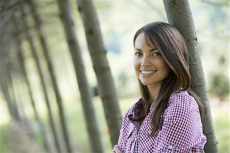 simsearch:6118-07235278,k - A woman standing in an avenue of trees, smiling. Foto de stock - Royalty Free Premium, Número: 6118-07235124