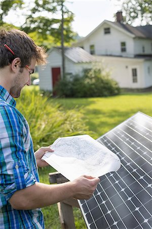 questões ambientais - A man using a plan to place a solar panel in a farmhouse garden. Foto de stock - Royalty Free Premium, Número: 6118-07235244