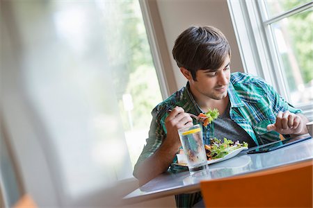 eating - A young man using a digital tablet. Stock Photo - Premium Royalty-Free, Code: 6118-07351160