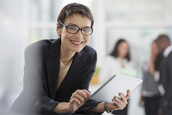 An office interior. A woman in a black jacket using a digital tablet. Stock Photo - Premium Royalty-Free, Image code: 6118-07351358