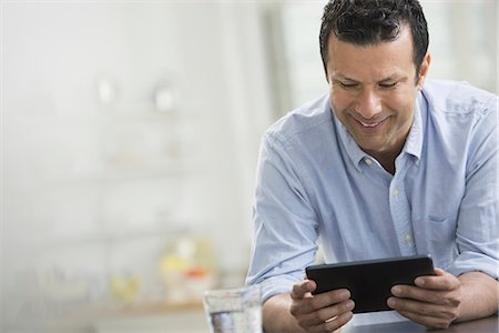 A man in a blue shirt leaning on a desk, holding a digital tablet. Stockbilder - Premium RF Lizenzfrei, Bildnummer: 6118-07351369