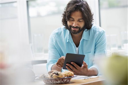 simsearch:6118-07351469,k - An office or apartment interior in New York City. A bearded man in a turquoise shirt using a digital tablet. Stock Photo - Premium Royalty-Free, Code: 6118-07351378