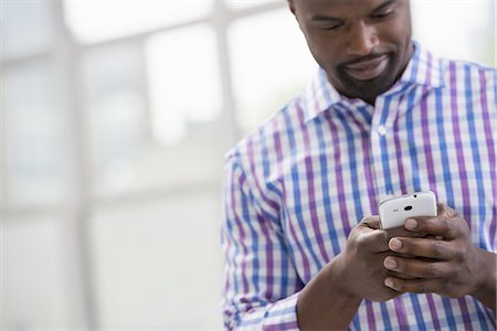 smart phone and texting and business and city - Professionals in the office. A light and airy place of work. A man in a checked shirt using a smart phone. Stock Photo - Premium Royalty-Free, Code: 6118-07351467