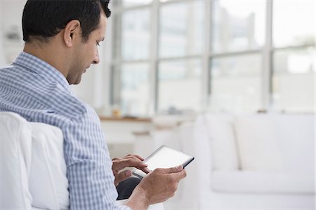 side view of someone sitting in chair - Professionals in the office. A light and airy place of work. A man seated using a digital tablet. Stock Photo - Premium Royalty-Free, Code: 6118-07351469