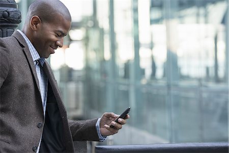 phone african american adults - Business people in the city. Keeping in touch on the move. A man standing outdoors checking his cell phone. Stock Photo - Premium Royalty-Free, Code: 6118-07351493