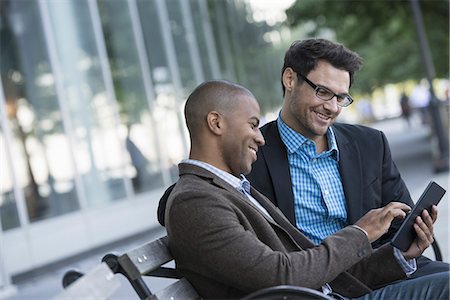 shaved head - Business people in the city. Keeping in touch on the move. Two men seated on a park bench outdoors, looking at a digital tablet. Stock Photo - Premium Royalty-Free, Code: 6118-07351490