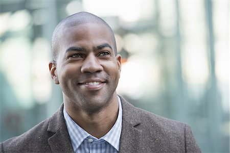 Business people in the city. Keeping in touch on the move. A man in jacket and tie smiling and looking into the distance. Stock Photo - Premium Royalty-Free, Code: 6118-07351495