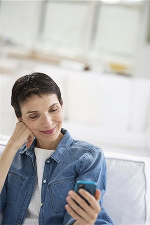 An open plan office in New York City. A mature woman with grey hair, wearing a denim shirt, looking at the screen of a smart phone. Stock Photo - Premium Royalty-Free, Code: 6118-07351433