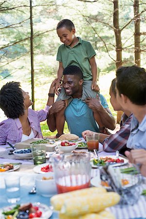 picnic table - A family picnic meal in the shade of tall trees. A young boy sitting on his father's shoulders. Stock Photo - Premium Royalty-Free, Code: 6118-07351553