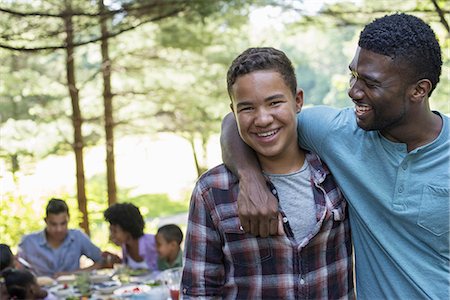 A family picnic meal in the shade of tall trees. A man and a young boy looking at the camera. Stock Photo - Premium Royalty-Free, Code: 6118-07351559