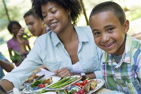 A family picnic meal in the shade of tall trees. Parents and children helping themselves to fresh fruits and vegetables. Foto de stock - Sin royalties Premium, Código: 6118-07351537