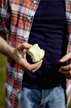 Mid section of a man wearing a plaid shirt, holding a half eaten apple. Stock Photo - Premium Royalty-Free, Code: 6118-07351645