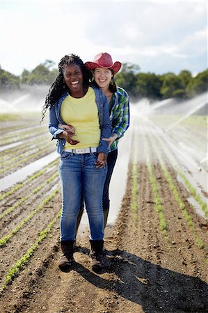 Two young women standing in a field of small seedlings, with the irrigation sprinklers spraying the ground. Foto de stock - Sin royalties Premium, Código: 6118-07351656