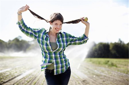 A girl in a green checked shirt with braids standing in a field with sprinklers working in the background. Foto de stock - Sin royalties Premium, Código: 6118-07351664