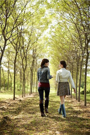 Two friends walking along a path through an avenue of trees. Stock Photo - Premium Royalty-Free, Code: 6118-07351621