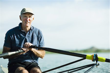 A middle-aged man rowing a single scull rowing boat on the water. Stock Photo - Premium Royalty-Free, Code: 6118-07351863