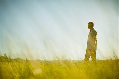 simsearch:6118-07351872,k - A man standing in grassland, looking into the distance. Foto de stock - Royalty Free Premium, Número: 6118-07351891