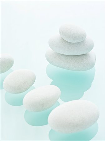 Smooth white pebbles of uniform size and colour displayed on a blue reflective glass background. Photographie de stock - Premium Libres de Droits, Code: 6118-07351993