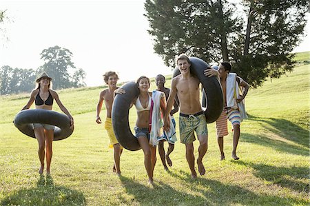 A group of young people, boys and girls, holding towels and swim floats, going for a swim. Foto de stock - Royalty Free Premium, Número: 6118-07351921