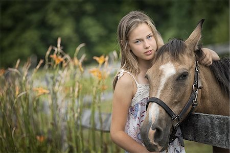 A young girl with a pony wearing a halter, in a field full of wild flowers and grasses. Stock Photo - Premium Royalty-Free, Code: 6118-07352049