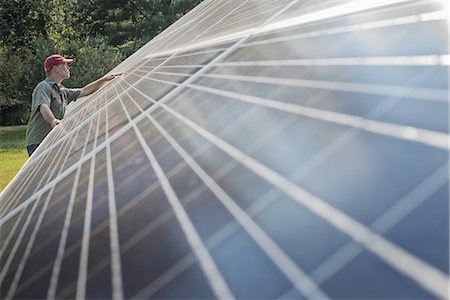 sustainable agriculture - A man inspecting the surface of a large tilted solar panel installation for harnessing the energy of the sun. Stock Photo - Premium Royalty-Free, Code: 6118-07352083