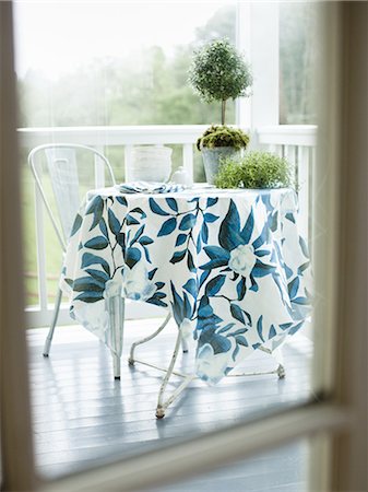 porch - A wrought iron round table and chair on a white painted house porch, with a blue patterned tablecloth. Stock Photo - Premium Royalty-Free, Code: 6118-07352004