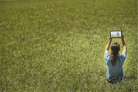 simsearch:6118-07203902,k - View from above of a woman sitting on grass, lifting up a personal computer notepad, looking at an image. Stock Photo - Premium Royalty-Free, Code: 6118-07352019