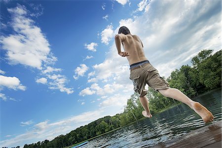 A boy taking a running jump into a calm pool of water, from a wooden jetty. Stock Photo - Premium Royalty-Free, Code: 6118-07352026