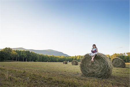 sunset farm - A field full of tall rounded hay bales, and a young girl sitting on the top of one large bale. Stock Photo - Premium Royalty-Free, Code: 6118-07352033