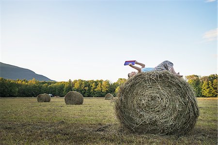 simsearch:6118-07203196,k - A field full of tall rounded hay bales, and a young girl sitting on the top of one large bale. Photographie de stock - Premium Libres de Droits, Code: 6118-07352034