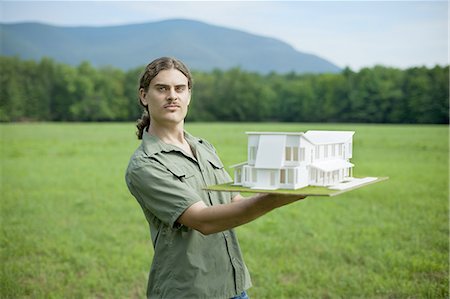 A rural scene and mountain range, and a person holding a scale model of a new building. Stock Photo - Premium Royalty-Free, Code: 6118-07352226