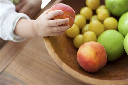 A small child, a one year old girl, grasping fruit from a bowl. Photographie de stock - Premium Libres de Droits, Code: 6118-07352396