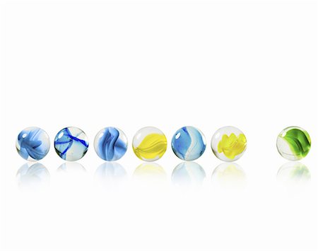 A row of glass marbles of different patterns and colours, with one separated from the rest. Stock Photo - Premium Royalty-Free, Code: 6118-07352319