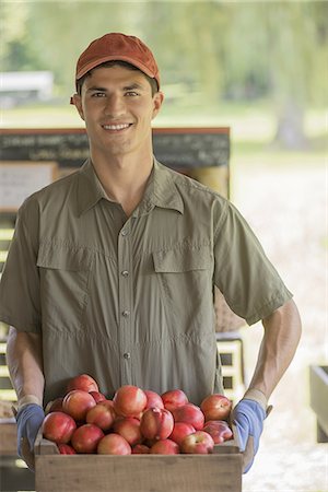 south american ethnicity - Organic farmer, young man holding baskets of fresh fruit at a market farm stand. Stock Photo - Premium Royalty-Free, Code: 6118-07352447