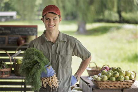 south american ethnicity - Organic farmer, young man holding baskets of fresh fruit at a market farm stand. Stock Photo - Premium Royalty-Free, Code: 6118-07352446