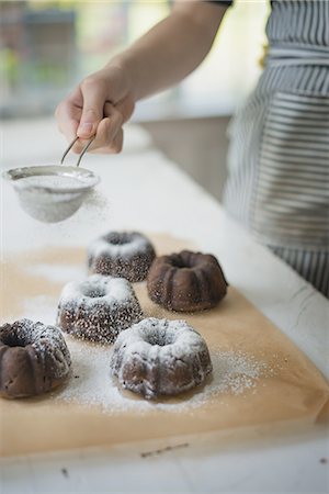 simsearch:6118-07354423,k - A woman dusting fresh made chocolate buns with icing sugar. Stock Photo - Premium Royalty-Free, Code: 6118-07352641