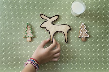 A girl's hand arranging an organic homemade Christmas cookies in the shape of a reindeer and Christmas trees. Stock Photo - Premium Royalty-Free, Code: 6118-07352973