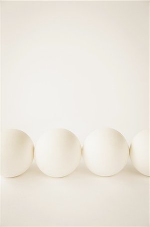 simsearch:6118-07353041,k - End-on view of free range, organic eggs with white shells arranged in a row, on a cream coloured background. Foto de stock - Royalty Free Premium, Número: 6118-07353042