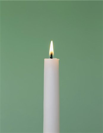 A thin white wax candle with a small  lit flame with a green background. Stock Photo - Premium Royalty-Free, Code: 6118-07353289