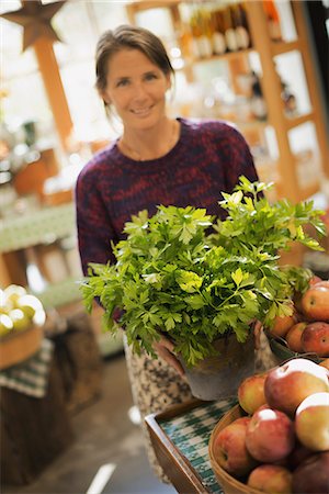 Organic Farmer at Work. A woman working ona farm stand, witha  display of fresh produce. Green plants and bowls of apples. Stock Photo - Premium Royalty-Free, Code: 6118-07353346
