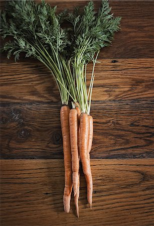 A small bunch of carrots with green leafy tops freshly harvested, lying on a tabletop. Stock Photo - Premium Royalty-Free, Code: 6118-07353354