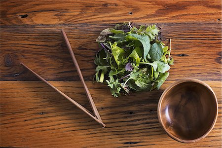 A small round polished wooden bowl and a clutch of organic mixed salad leaves, with wooden chopsticks. Photographie de stock - Premium Libres de Droits, Code: 6118-07353358