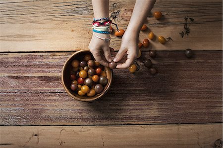 point of view hands - A round bowl with small tomatoes of various colours, and a person sorting and picking over them. A wooden tabletop. Stock Photo - Premium Royalty-Free, Code: 6118-07353360