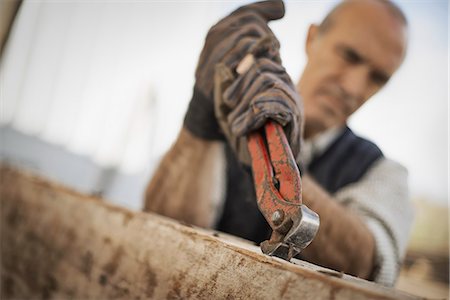 A man working in a reclaimed timber yard. Using a tool to remove metals from a reclaimed piece of timber. Stock Photo - Premium Royalty-Free, Code: 6118-07353388