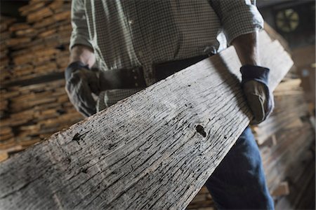 A heap of recycled reclaimed timber planks of wood. Environmentally responsible reclamation in a timber yard. A man carrying a large plank of mature weathered wood. Foto de stock - Sin royalties Premium, Código: 6118-07353397