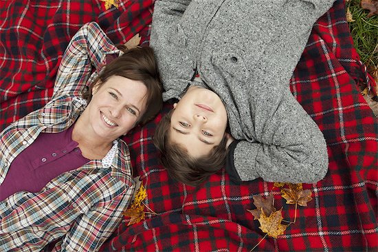 Two people, a woman and a child, lying on a red tartan picnic blanket, looking upwards. Stock Photo - Premium Royalty-Free, Image code: 6118-07353443