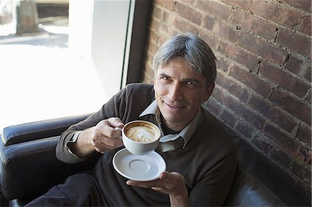 A man sitting in a coffee shop. Holding a cup of frothy  cappuccino coffee. Photographie de stock - Premium Libres de Droits, Code: 6118-07353460